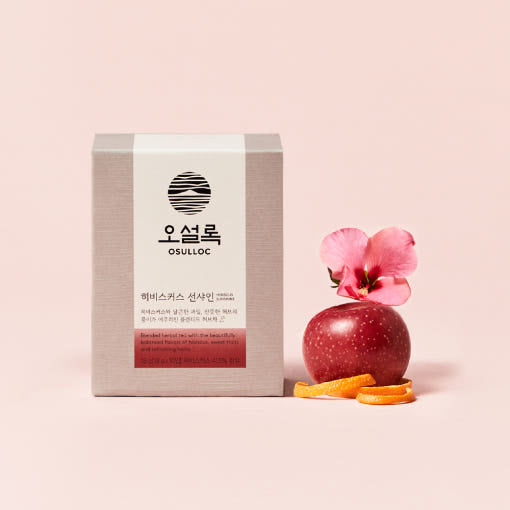 Boîte rose pâle OSULLOC Hibiscus Sunshine Tea avec une fleur d'hibiscus et une pomme rouge à côté du packaging.