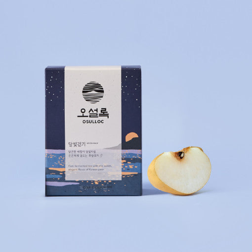 Boîte bleue étoilée OSULLOC Moon Walk Tea posée à côté d'une tranche de poire coréenne fraîche.