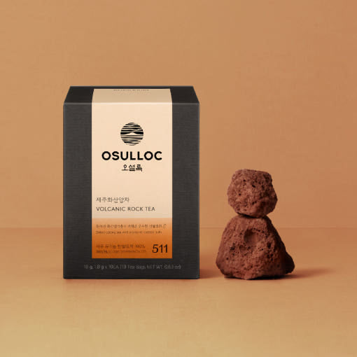 Boîte noire OSULLOC Volcanic Rock Tea à côté d'une pierre volcanique sculptée sur un fond ocre chaleureux.