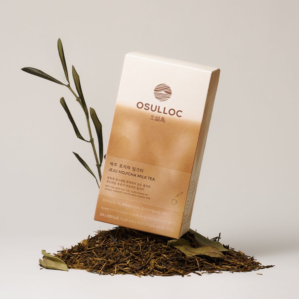 Boîte OSULLOC Hojicha Milk Tea posée sur des feuilles de hojicha torréfiées