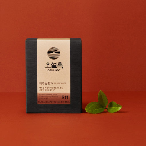 Boîte de thé noir Jeju Forest OSULLOC sur fond terre de sienne avec feuilles de thé fraîches.