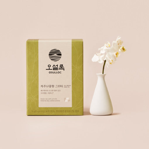 Boîte verte OSULLOC Jeju Orchid Green Tea à côté d'un vase blanc contenant une orchidée délicate.
