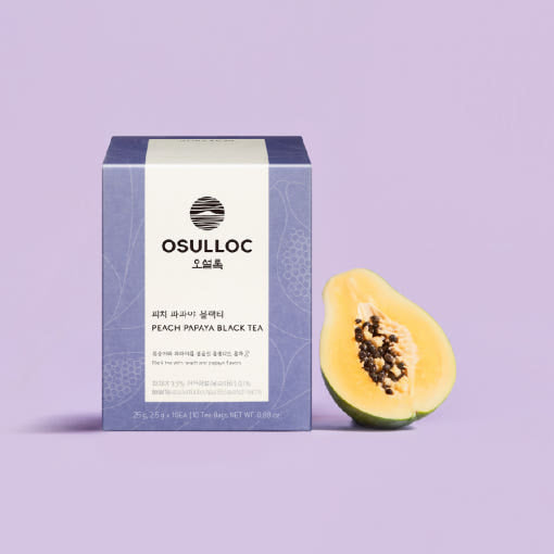 Boîte violette OSULLOC Peach Papaya Black Tea posée à côté d'une papaye fraîche coupée en deux.