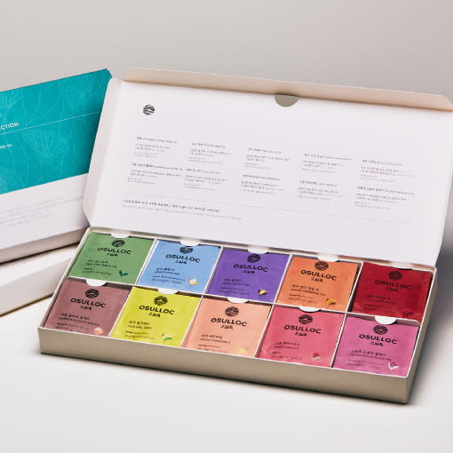 Grand coffret ouvert OSULLOC montrant 40 sachets de thé colorés organisés par saveurs dans un écrin blanc élégant.