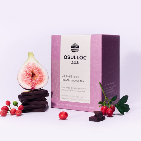 Boîte violette OSULLOC Fig Apple Black Tea à côté d'une figue ouverte, de tranches de pomme et de carrés de chocolat noir.