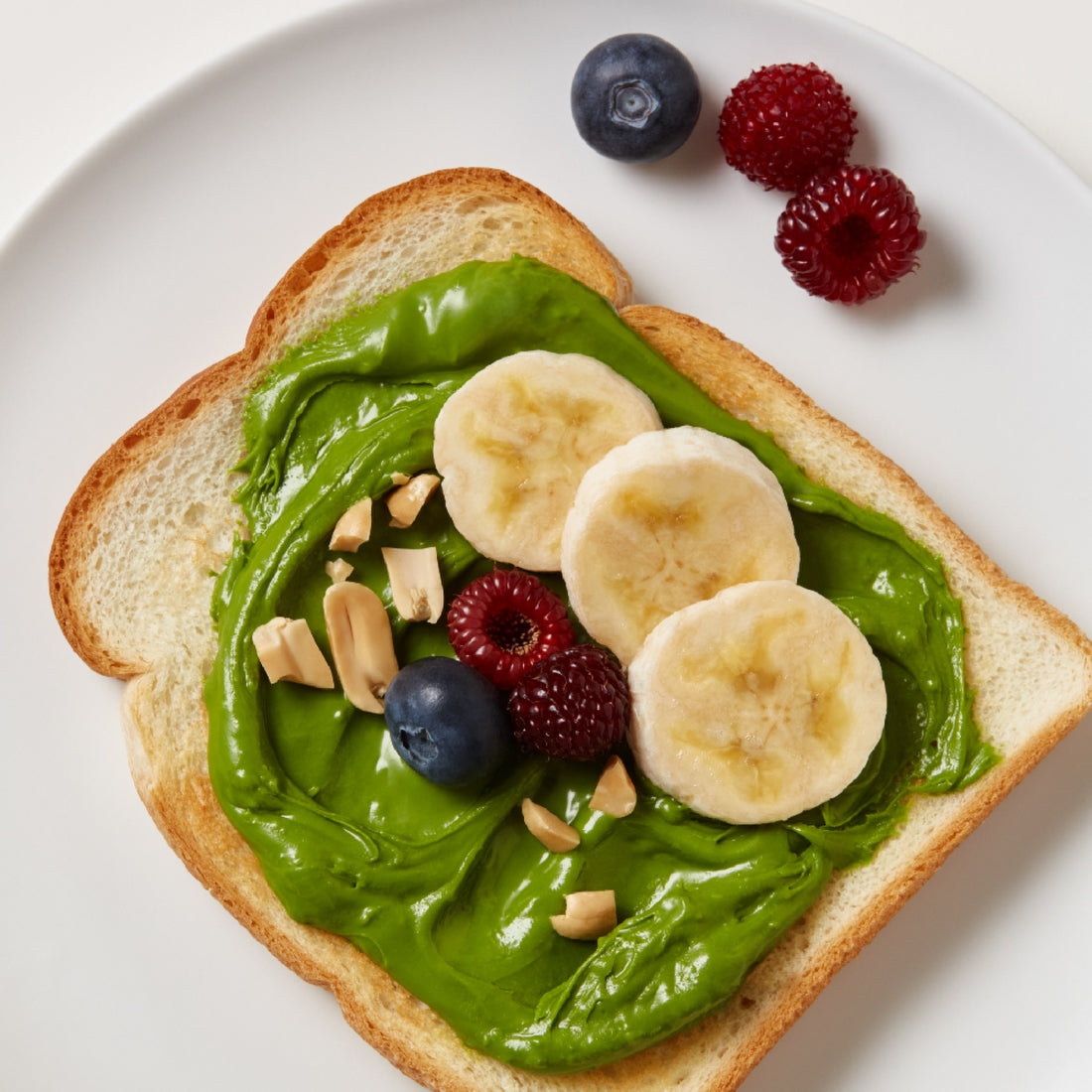 Pot de OSULLOC Green Tea Milk Spread Pâte à Tartiner au Thé Vert à côté de biscuits nappés de crème verte et d'une tartine à la banane.