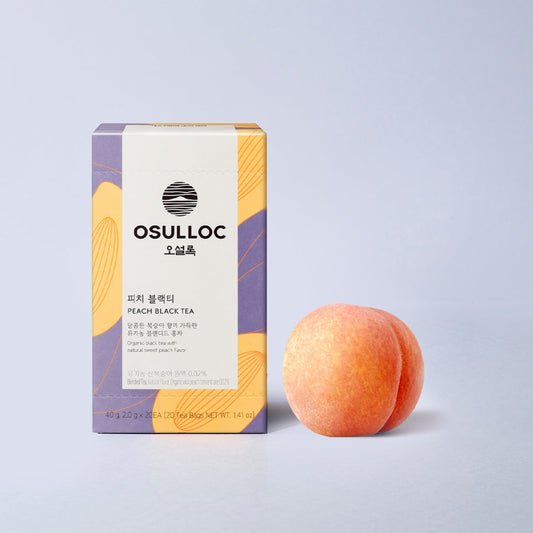 Boîte violette et jaune de OSULLOC Peach Black Tea  à côté d'une pêche fraîche entière.