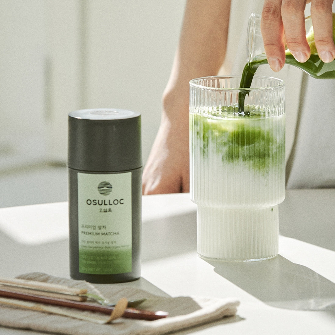 Boîte grise élégante et pot de OSULLOC Premium Matcha 40g avec poudre vert émeraude et préparation de latte au matcha.