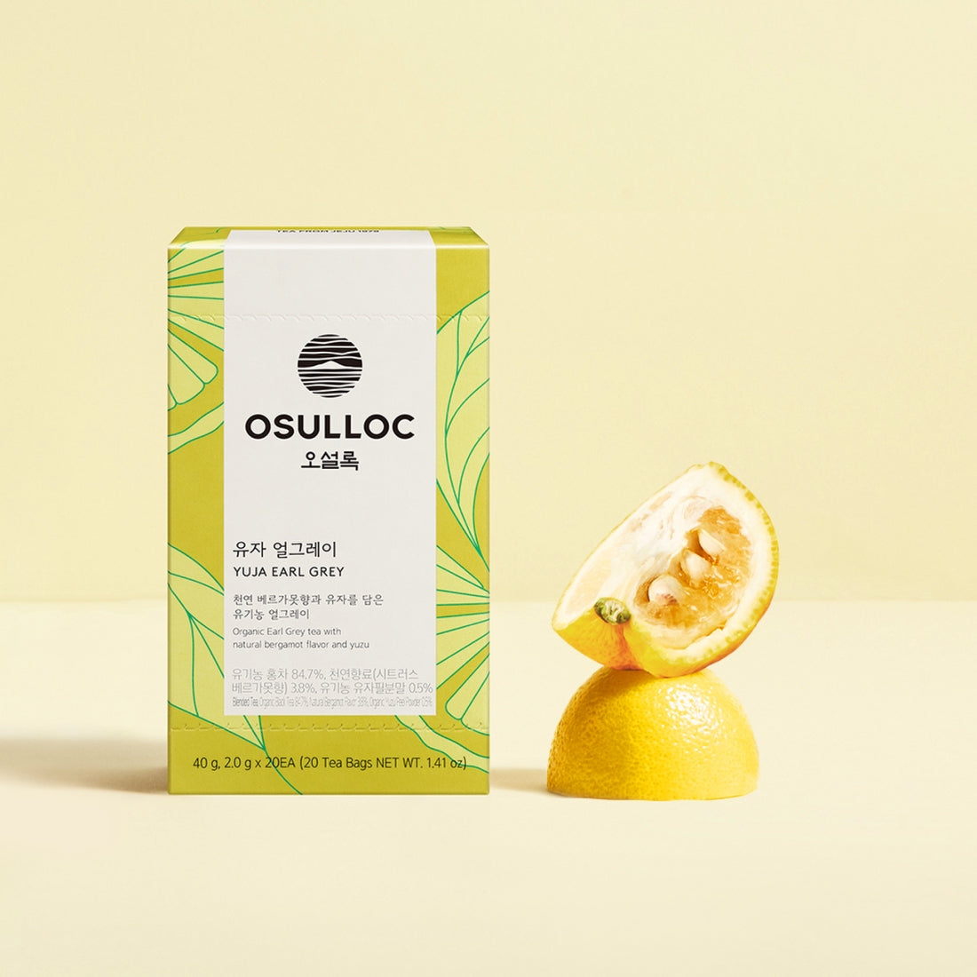 Boîte jaune et verte OSULLOC Yuja Earl Grey posée à côté d'un Yuzu coupé 