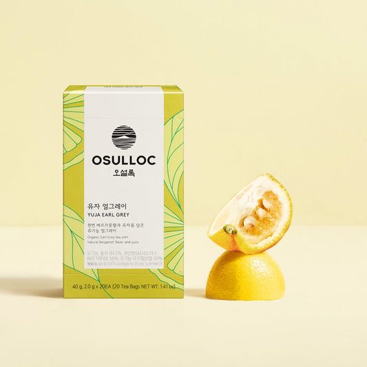 Boîte jaune et verte OSULLOC Yuja Earl Grey posée à côté d'un Yuzu coupé 