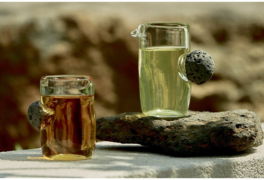 Thé infusé en verseuse et tasse en verre sur une pierre volcanique de Jeju